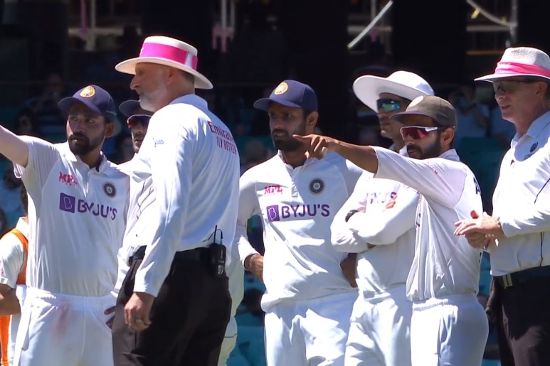 Indian players wearing white cricket kit point towards a section of the crowd