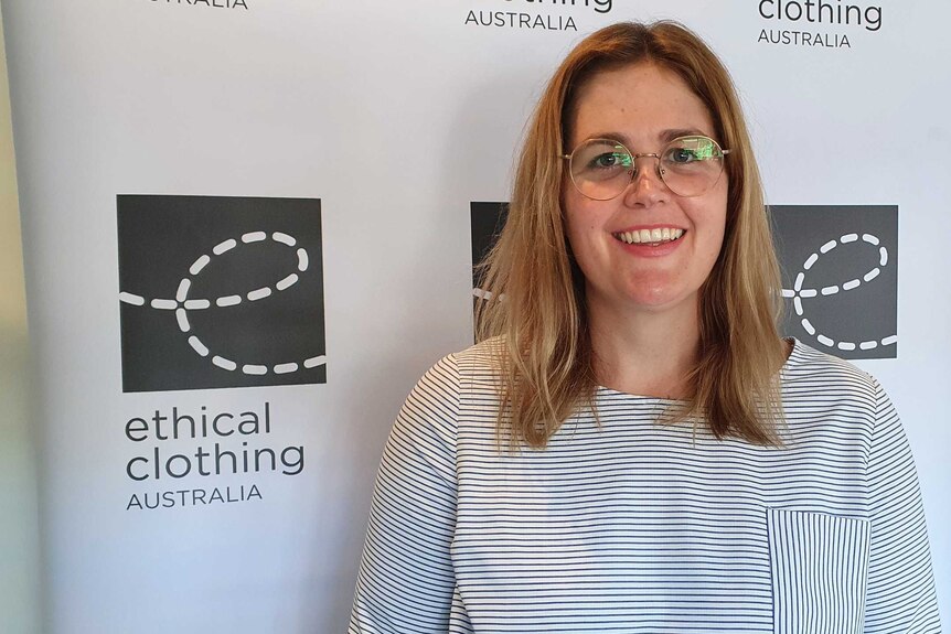 A woman wearing glasses standing in front of a banner says ethical clothing australia