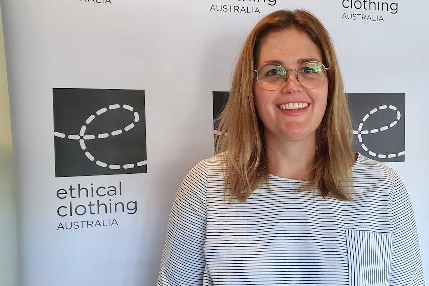 A woman wearing glasses standing in front of a banner says ethical clothing australia
