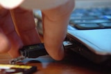Close-up TV still of a person inserting a DDA digital album on a USB stick into a laptop.