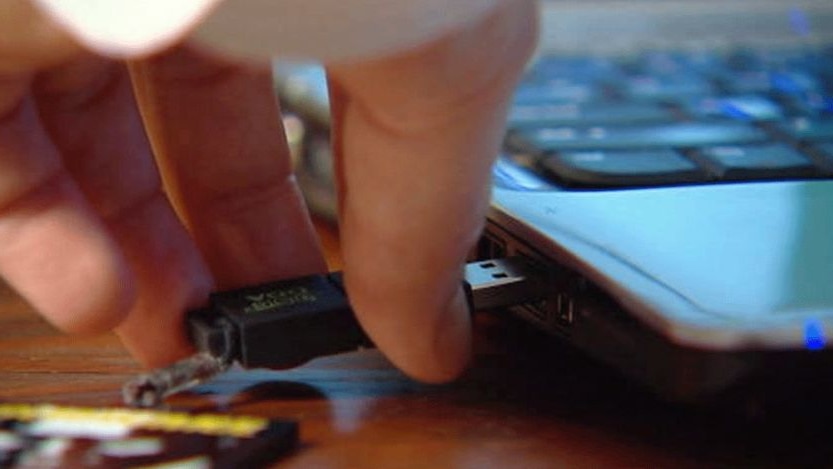 Close-up TV still of a person inserting a DDA digital album on a USB stick into a laptop.