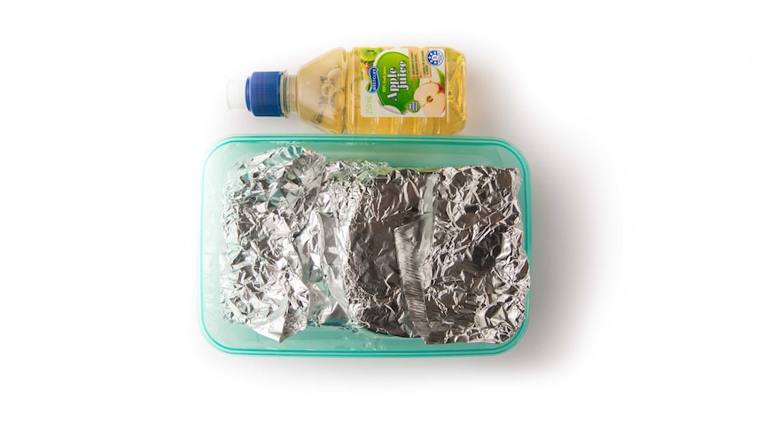 A jam sandwich wrapped in foil in a lunch box next to an apple fruit drink.