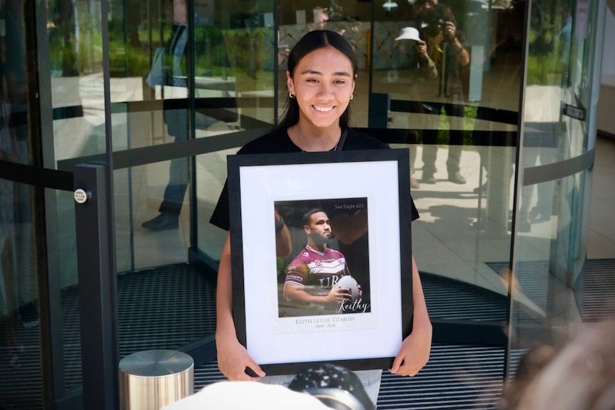 A girl holds a framed photo of Keith Titmuss