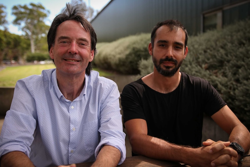 Two men sit outside a building.