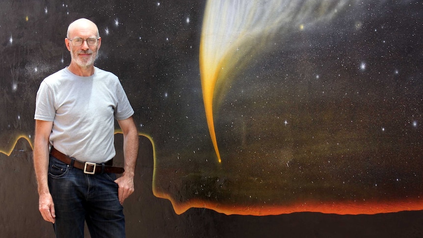 Retired astronomer Rob McNaught is pictured with a brightly coloured mural in Coonabarabran. The mural features Comet McNaught.
