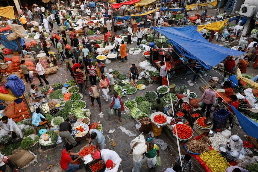 People shop at a crowded wholesale vegetable market in Delhi