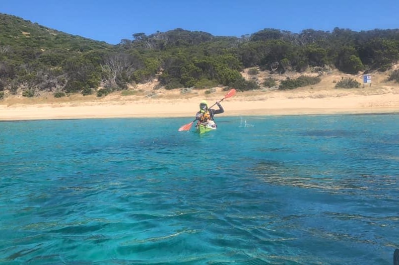 A man in a kayak with an island behind him.