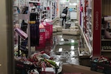 The inside of a shop after being flooded with water and debris on the floor and an employee trying to clean up.