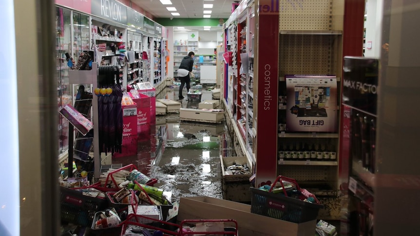 The inside of a shop after being flooded with water and debris on the floor and an employee trying to clean up.