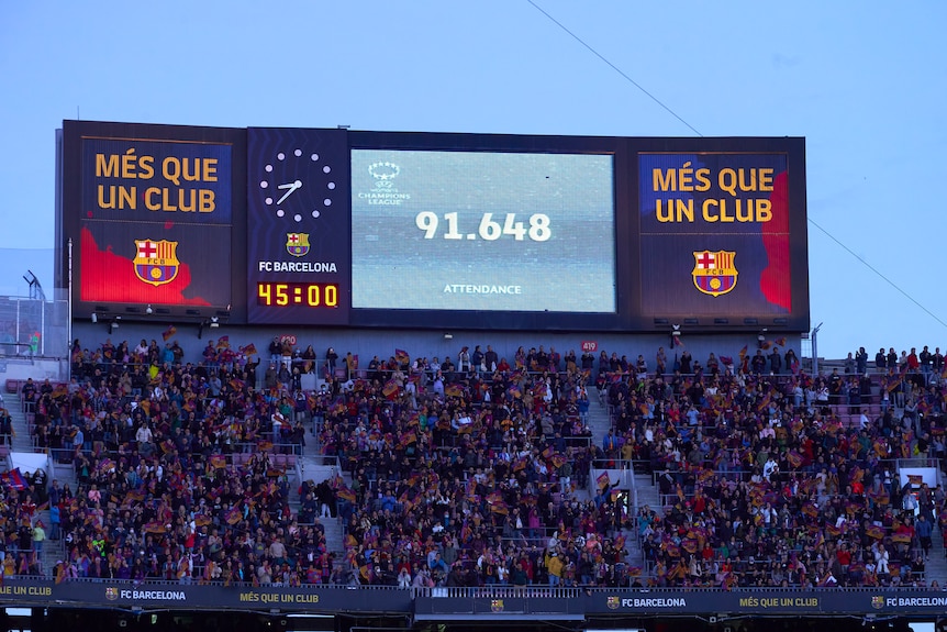 Un écran LED géant au sommet d'une tribune avec le logo du FC Barcelone affiche l'heure et un signe "91 648 participants".