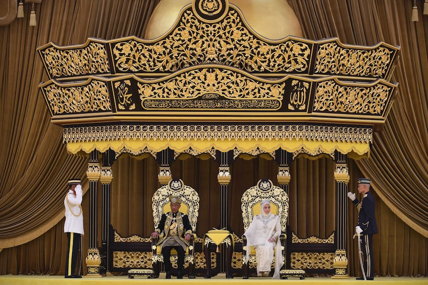 The new Malaysian king and queen sit on lavish thrones and sit under an elaborate canopy of estate