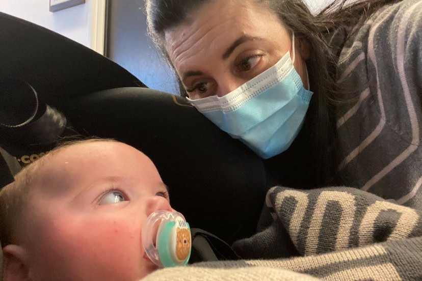 A mother with a face mask makes eye contact with her newborn.