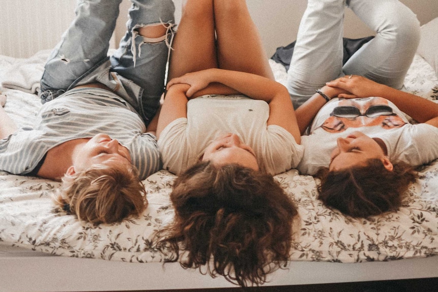 Three women lay on a bed with their legs in their air