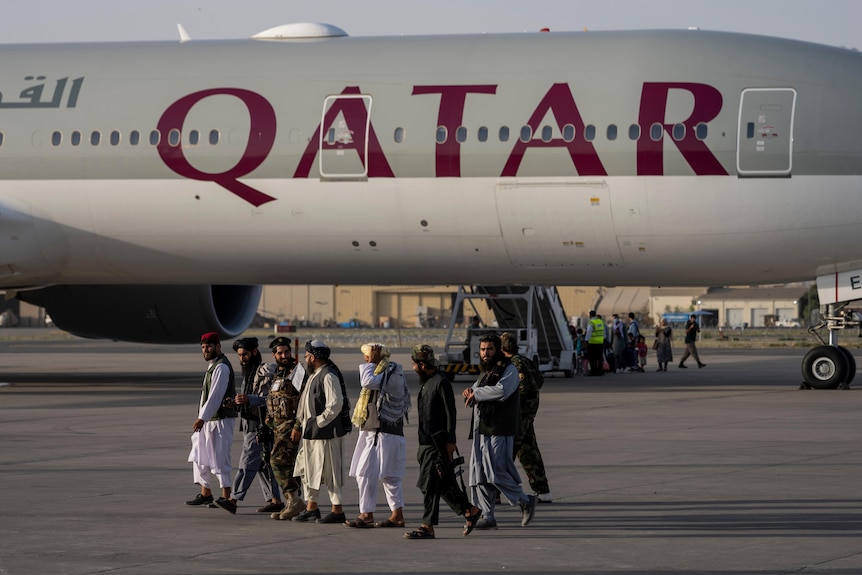 Taliban fighters walk past a Qatar Airways aircraft at the airport in Kabul