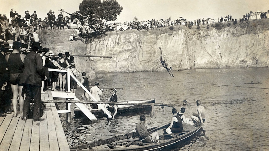 People stand on cliffs watching a swimmer dive into the water at Surrey Dive.