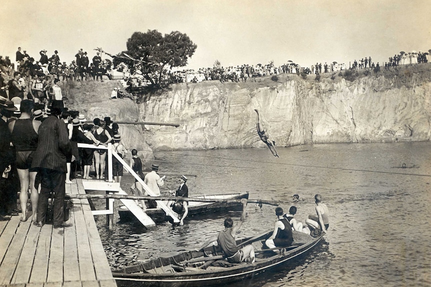People stand on cliffs watching a swimmer dive into the water at Surrey Dive.