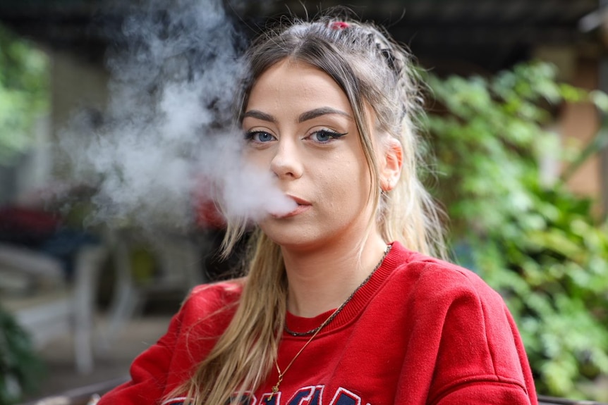 A young woman blows smoke out of her mouth