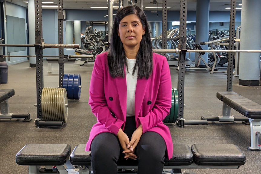 A woman in a pink jacket sitting in a gym.