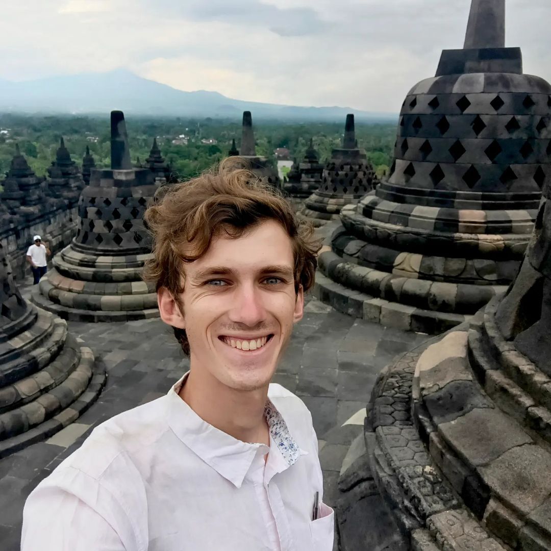 A man smiles in front of a landscape with temples.