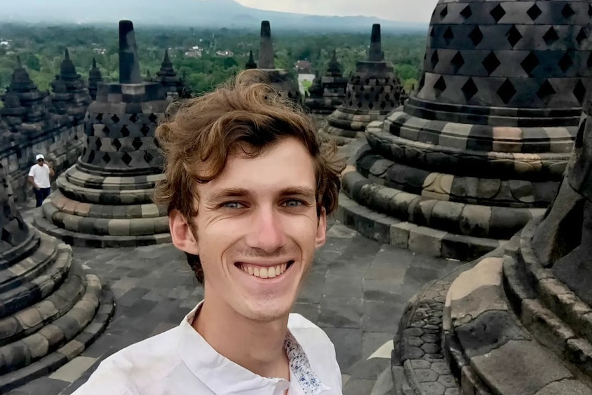 A man smiles in front of a landscape with temples.