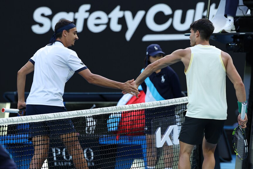 Two male tennis players meet at the net, touch hands, congratulating each other