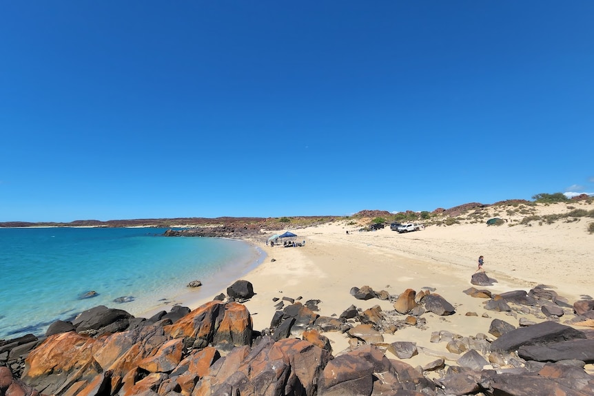 People hanging out at the beach next to bright blue water.