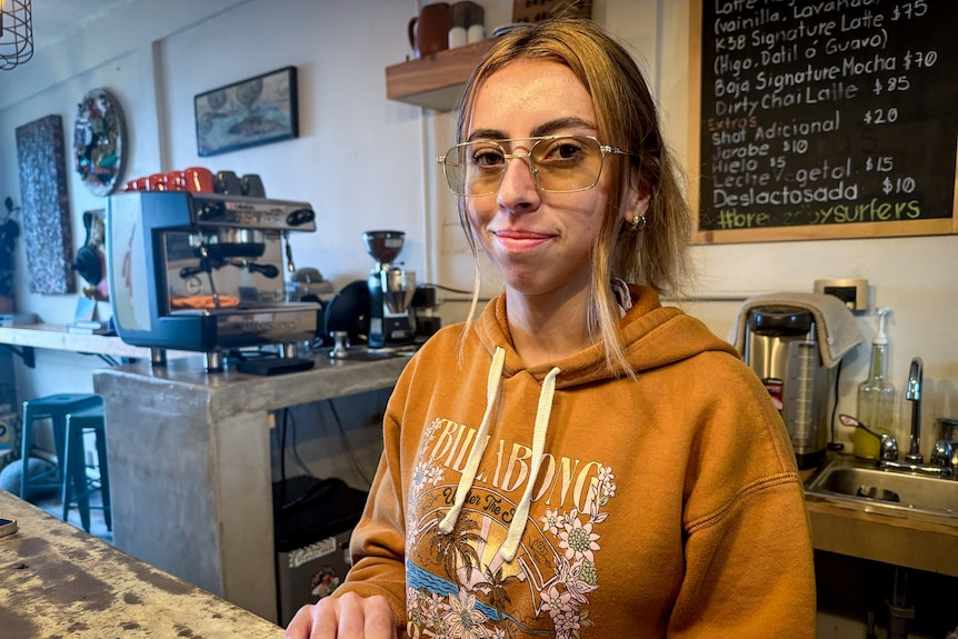 A woman in glasses and a Billabong hoodie stands at a coffee shop counter