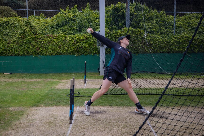 A woman bowls down a cricket pitch in the nets.