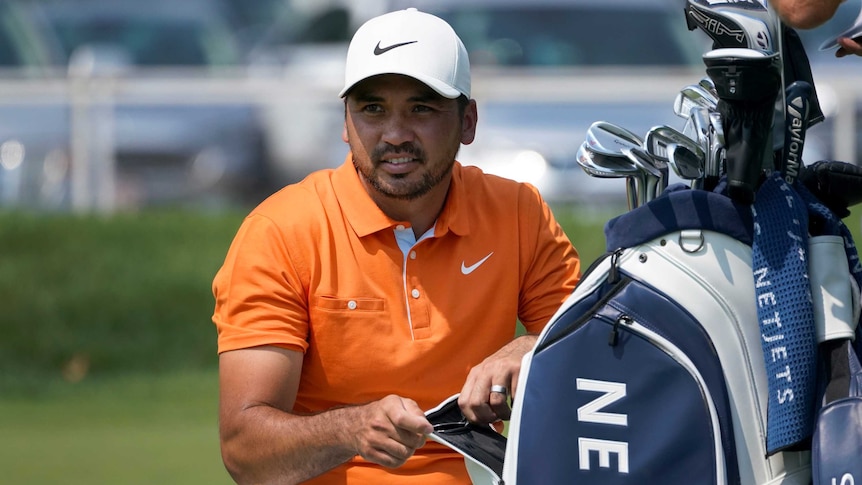 A professional golfer hunkers down next to his bag as he looks down the fairway.