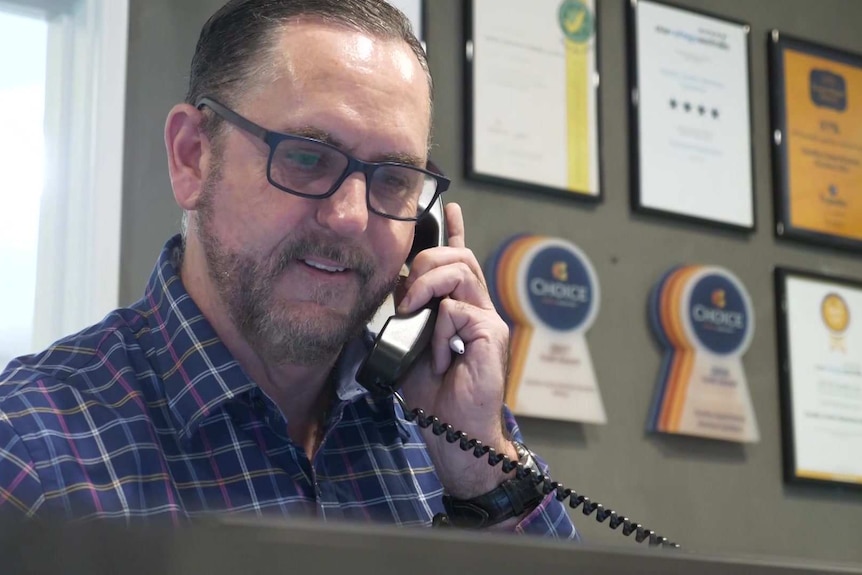 A man sits at a hotel reception and speaks on the phone