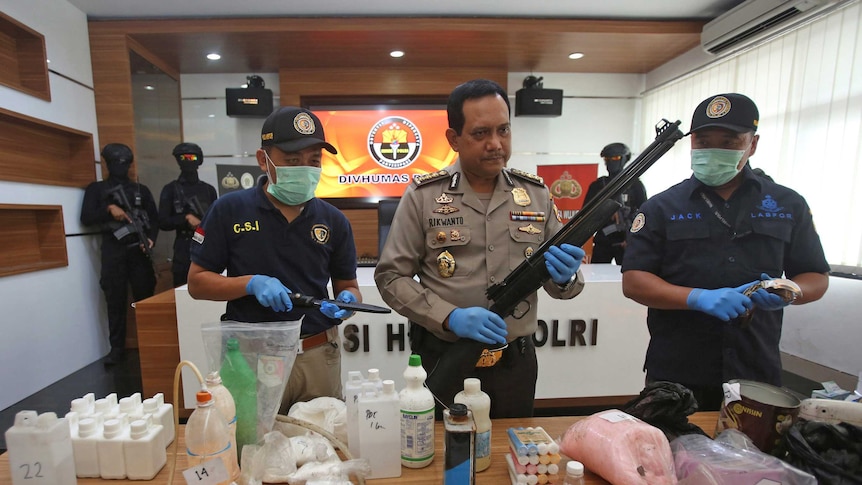 Policemen stand behind a table with weapons and other materials