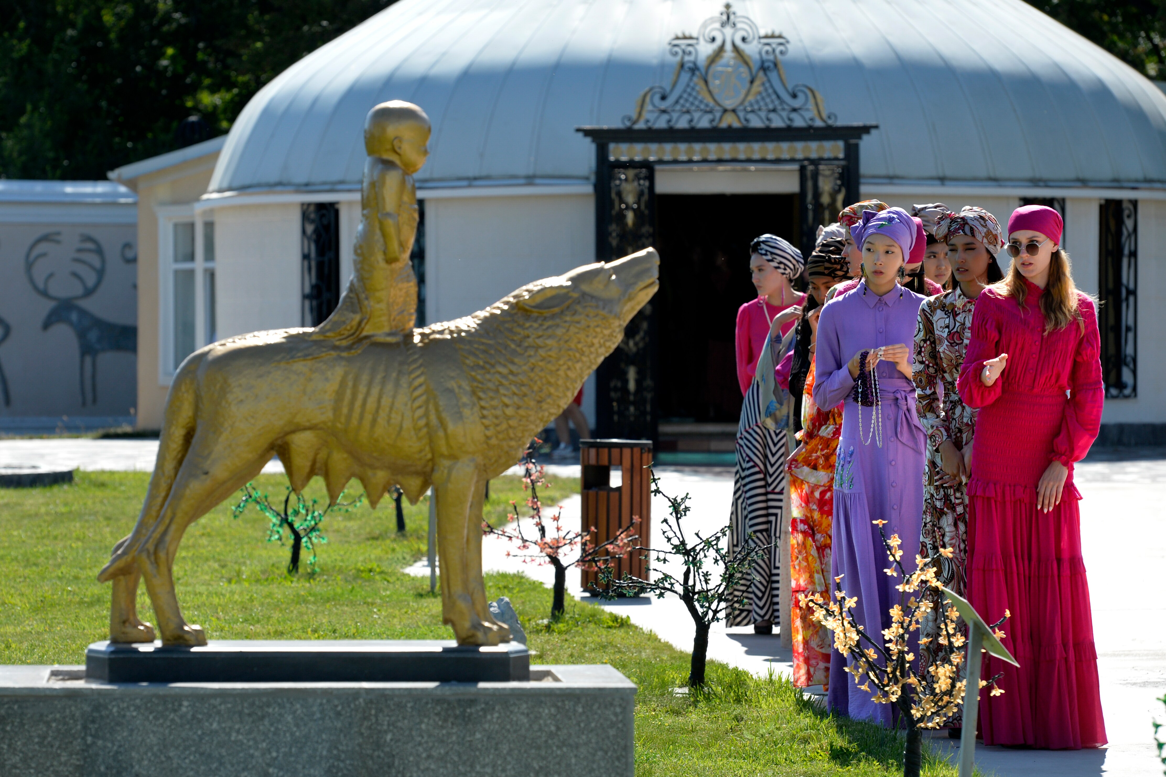 Models dressed in bright clothing are lined up next to a gold statue. 
