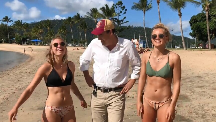 Jason Costigan Whitsunday MP with two women in bikinis at the beach.