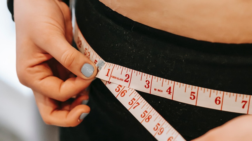 A woman in black tights measures her hips with a red measuring tape