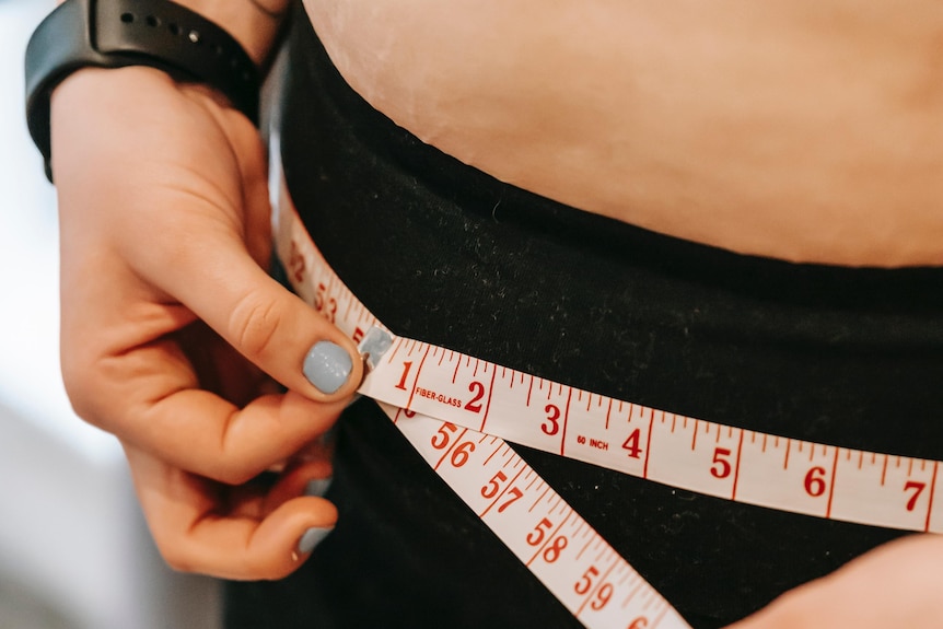 A woman in black tights measures her hips with a red measuring tape