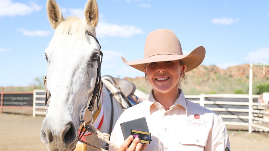 A woman smiles at the camera. She is standing next to a horse.