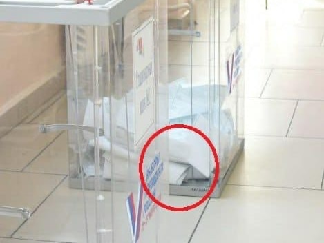 A pile of folded ballots at the base of a clear box.