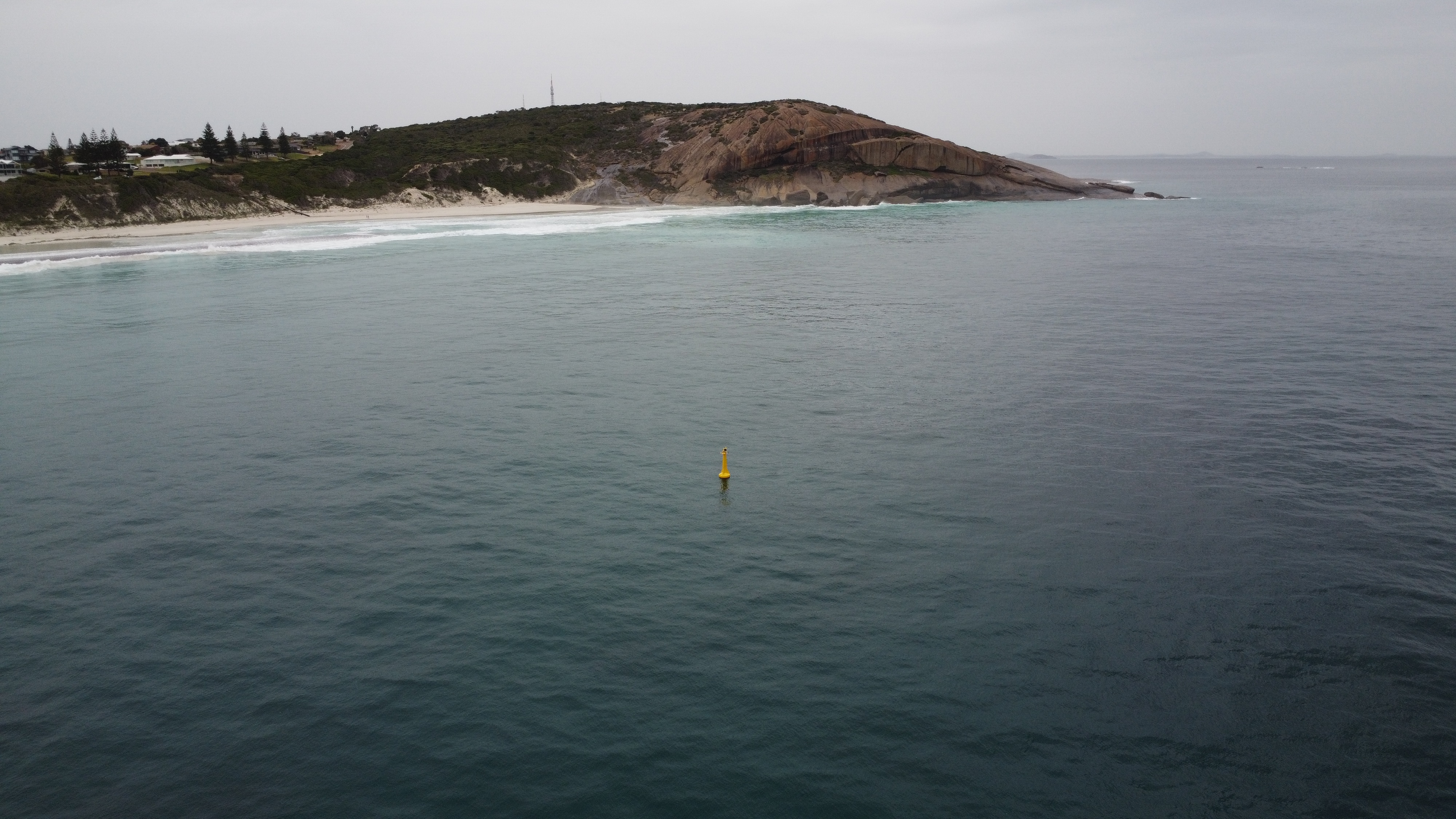 A yellow bouy in the ocean with land in the background