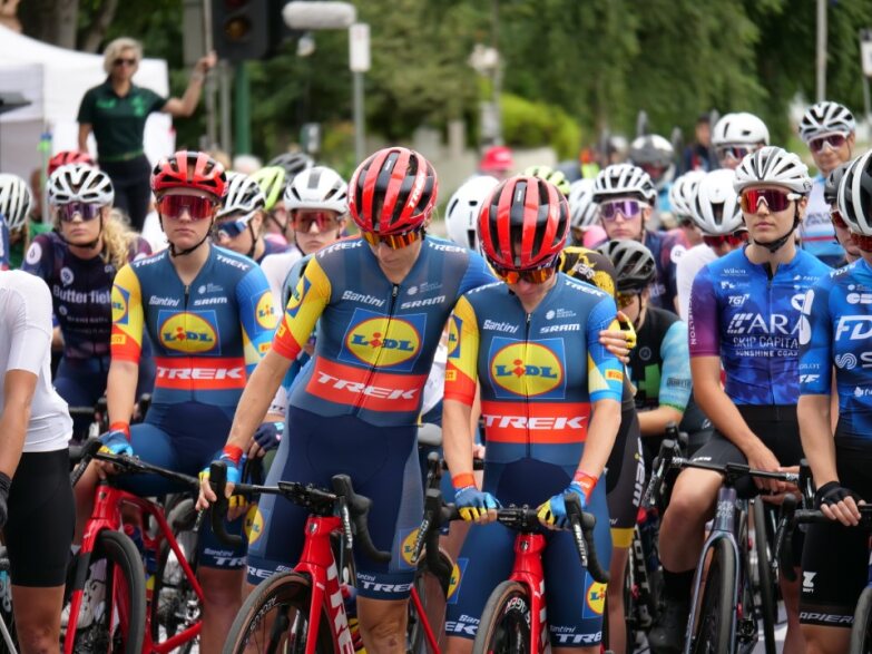 A group of cyclists sitting on their bikes looking solemn, one cyclist comforts another with an arm around the other. 