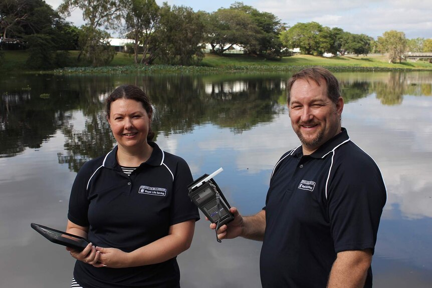 Researchers Amy Peden and Richard Franklin stand beside the Ross River in Townsville, he is holding a breathalyser.