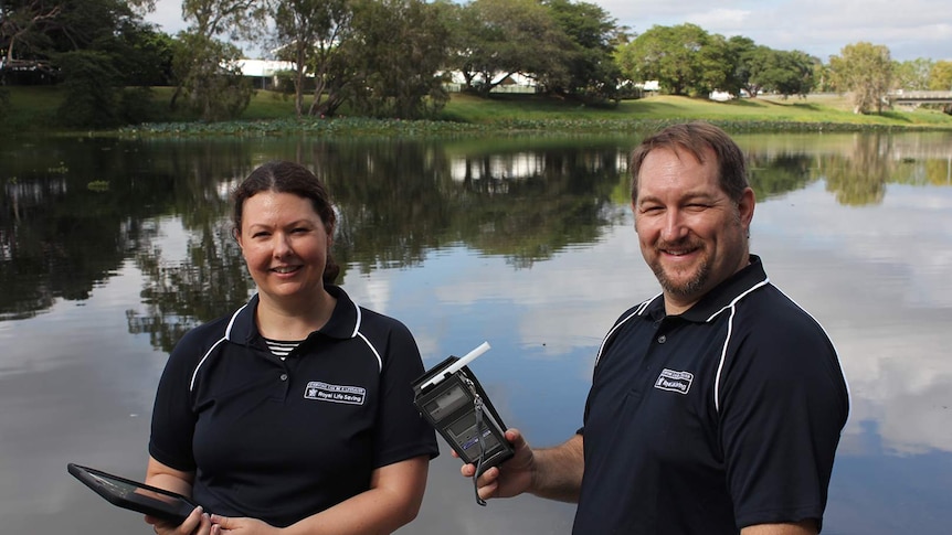 Researchers Amy Peden and Richard Franklin stand beside the Ross River in Townsville, he is holding a breathalyser.