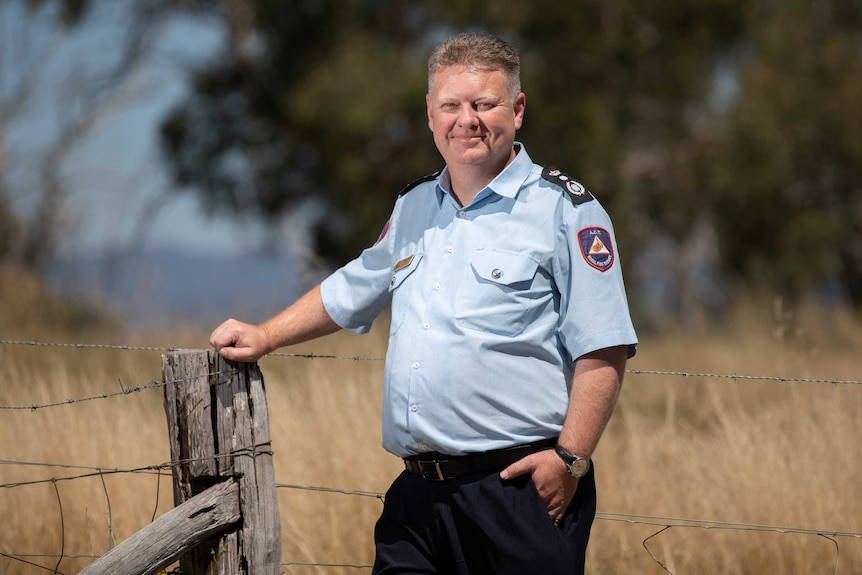 A uniformed Rohan Scott stands by a barbed wire fence.