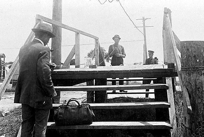Two men, standing either side of a small wooden footbridge, each holding a piece of string, pull a box between them.