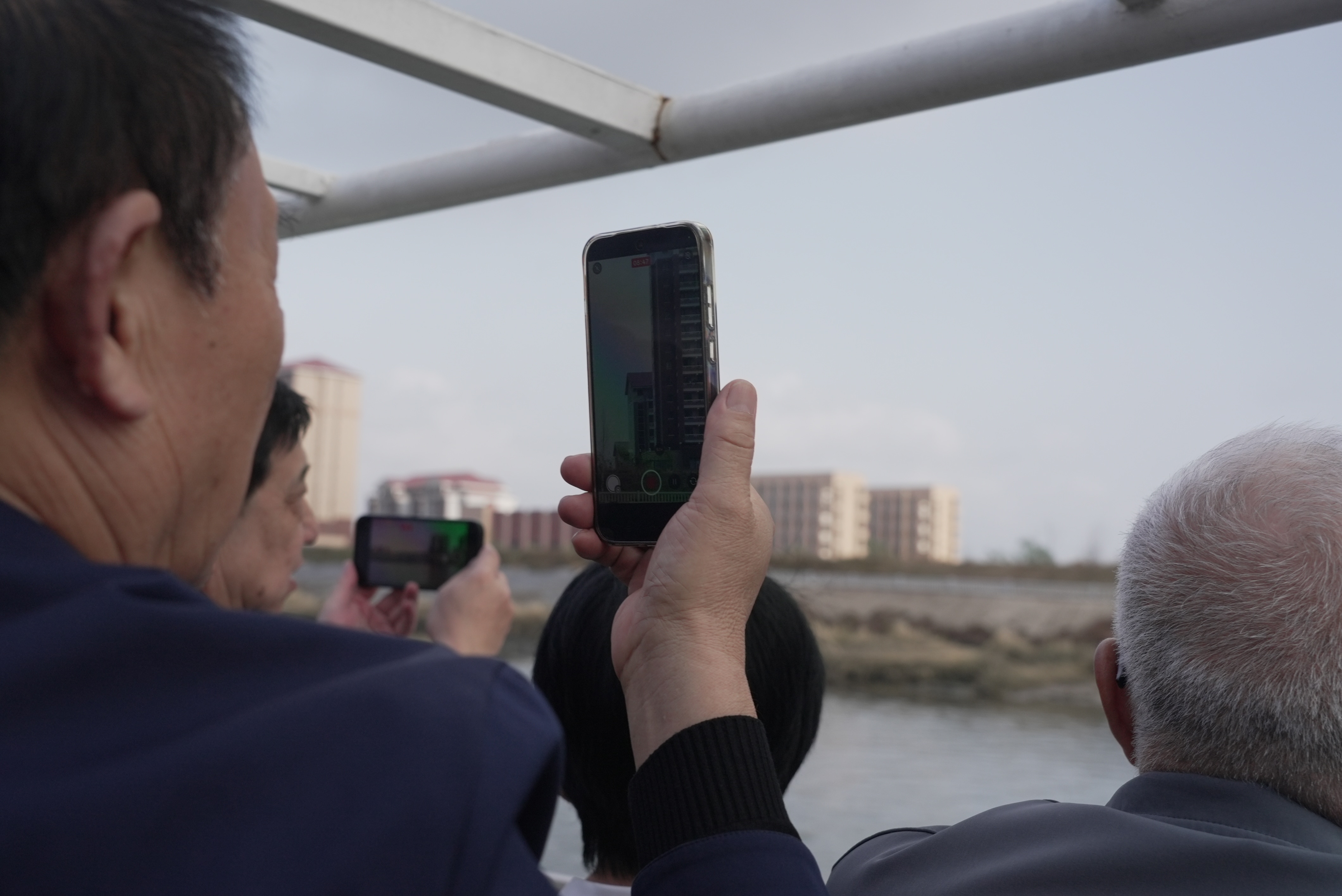 Tourists on a river cruise take capture footage of Sinuiju on their phones.