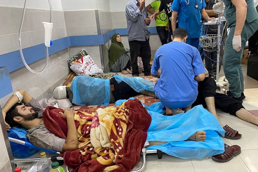 Several patients in a damaged hospital lying on the ground, as doctors attend to them.
