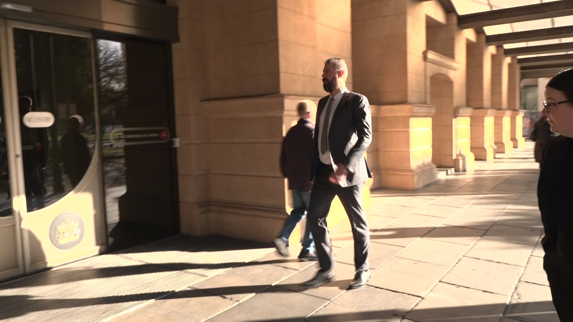 A tall man wearing a suit and tie walking towards an automatic door