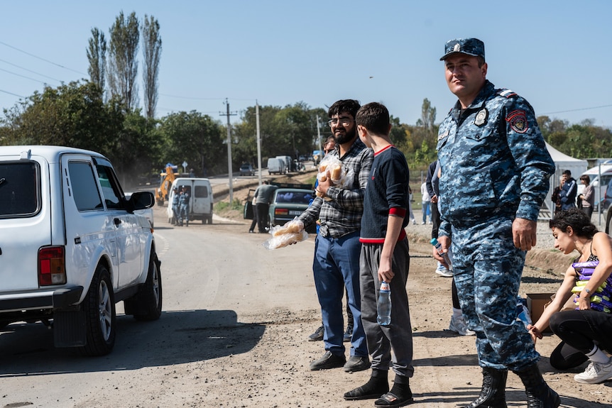 A man stands with a soldier handing out bread to passing refugees.