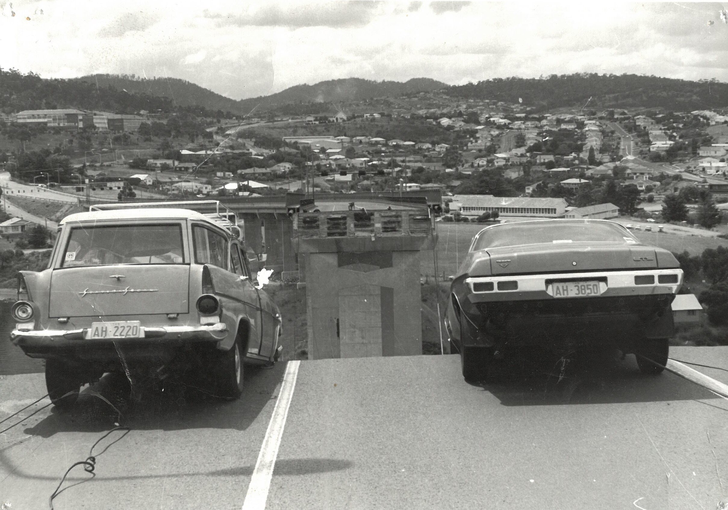 Two cars hang over the edge of a collapsed bridge section high in the air.