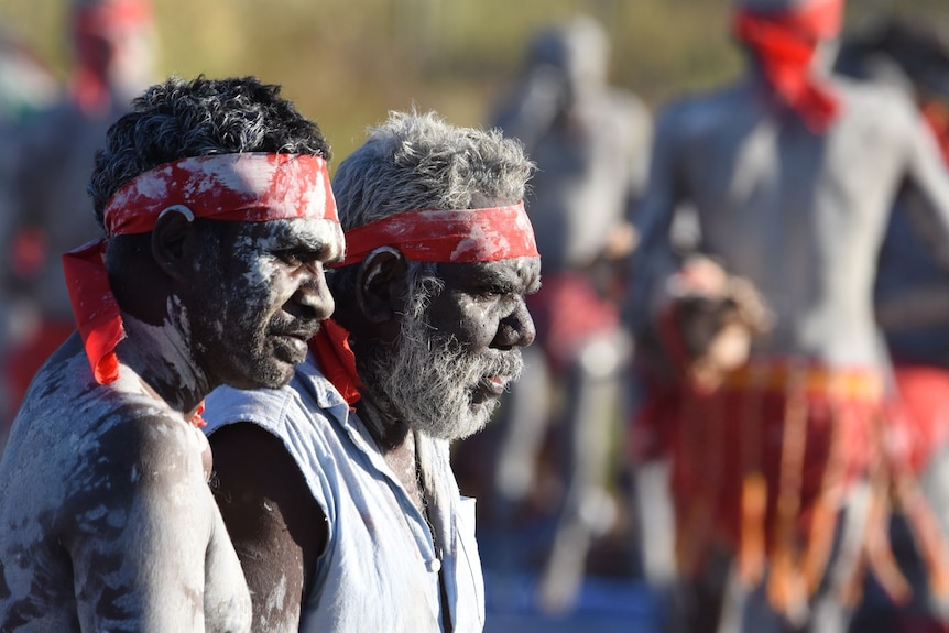 Two men wearing white face and body paint look into the distance at a traditional men's ceremony in Wadeye.