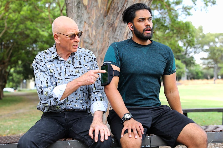 Dr Karl Kruszelnicki pretending to press play on a mobile phone on the arm of a runner listening to a podcast